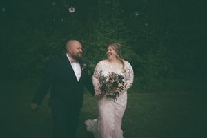 Smiling bride and groom walk together outdoors, bride wearing lace gown and holding bouquet.