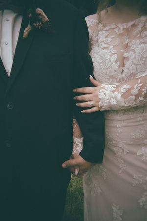 Close-up of bride in lace wedding gown holding grooms arm showing intricate floral lace sleeve detail.