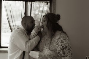 Black and white photo of groom feeding bride cake indoors near a bright window after wedding.