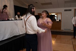 Couple dancing at wedding reception in banquet hall, woman in lavender bridesmaid dress.
