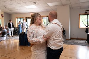 Bride and groom share first dance in lace wedding attire at indoor wedding reception venue.