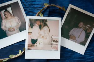 Three Polaroid photos of wedding moments displayed on blue wooden surface with greenery decoration.