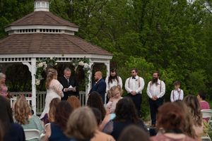 Outdoor wedding ceremony at white gazebo with guests seated and wedding party standing at altar.