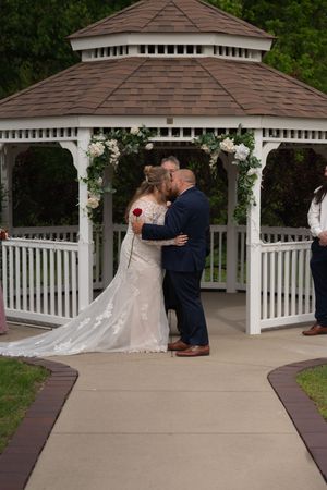 Bride and groom share their first kiss under a white floral gazebo during an outdoor wedding ceremony.