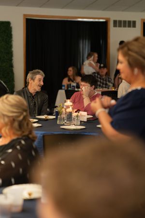 Wedding reception guests laugh and converse at candlelit tables in decorated banquet hall.