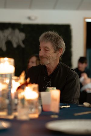 Elderly man with gray hair smiling at candlelit dinner table in dimly lit room.