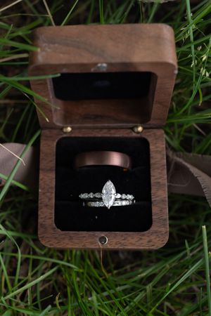Wedding rings displayed in open walnut wood box nestled in green grass outdoors.