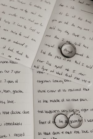 Handwritten wedding vows on paper with two engraved wedding bands reading always and I'm so grateful.