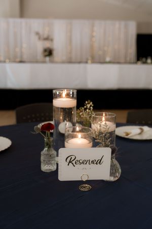 Reserved wedding reception table with floating candle centerpieces on navy tablecloth.