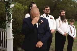 Emotional groom crying at the altar during outdoor wedding ceremony with groomsmen standing behind him.