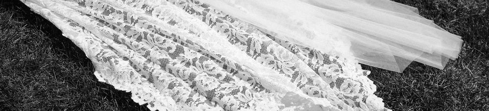 Black and white photo of elegant white lace wedding dress fabric laid on grass.