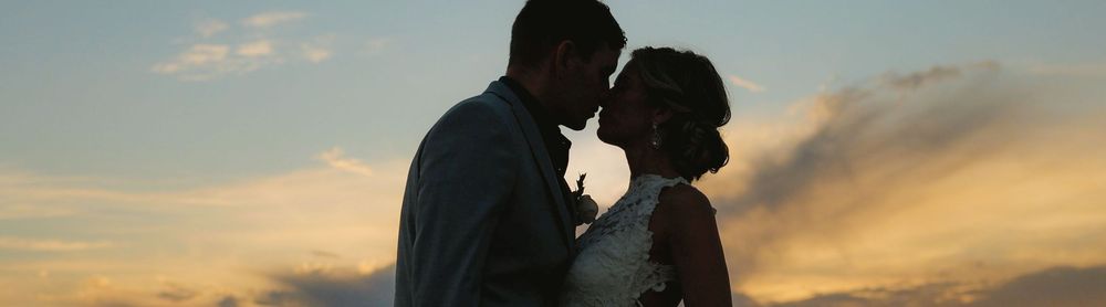 Romantic couple silhouetted against a vibrant sunset sky sharing an intimate moment.