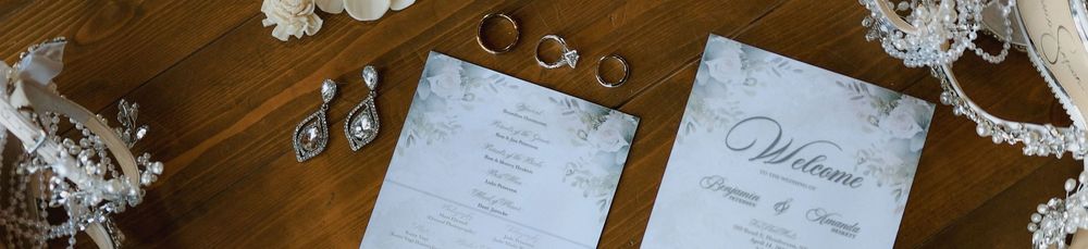 Elegant wedding stationery flat lay with welcome cards, gold rings, and crystal drop earrings on rustic wood.