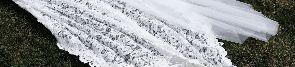 White lace wedding veil laid out on green grass, showcasing intricate floral lace trim detail.