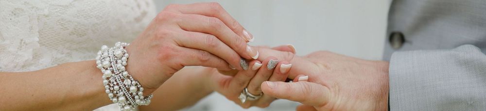 Close-up of a bride and groom exchanging wedding rings, bride wearing an elegant pearl and crystal bracelet.