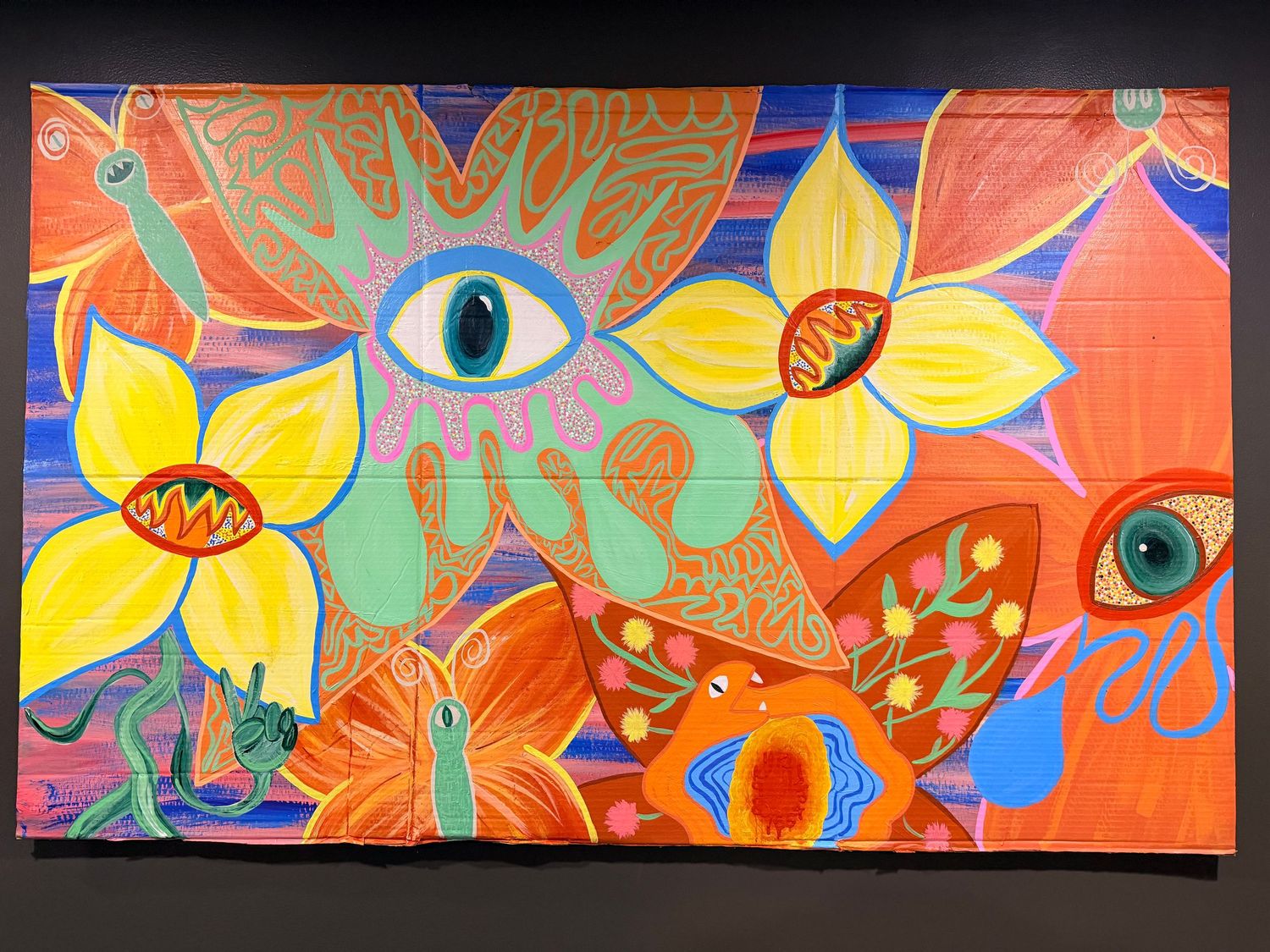 Vibrant psychedelic eye painting on black canvas with yellow, blue, and red abstract patterns in a wooden frame.