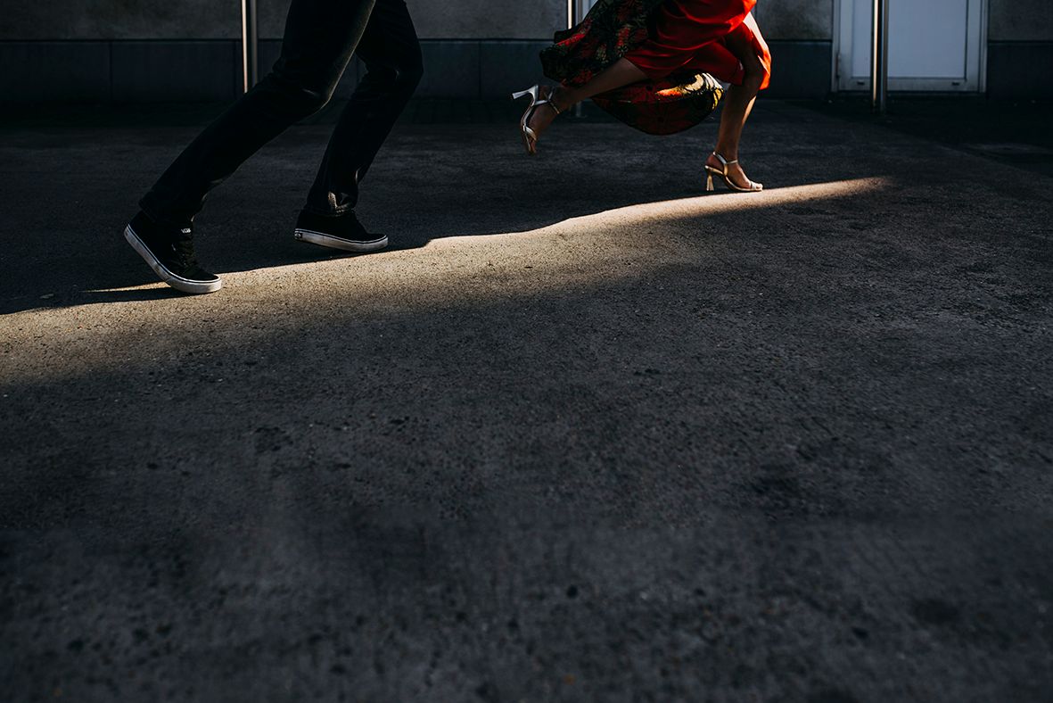 Couple walking in dramatic sunlight on pavement, woman in red dress, artistic shadow contrast.