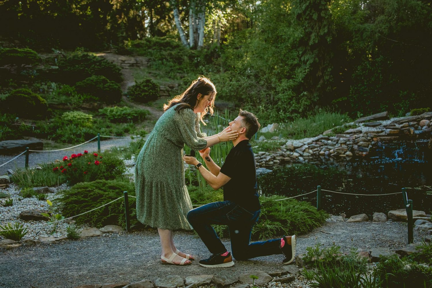 A couple poses romantically outdoors at golden hour, with warm sunset light glowing behind them.
