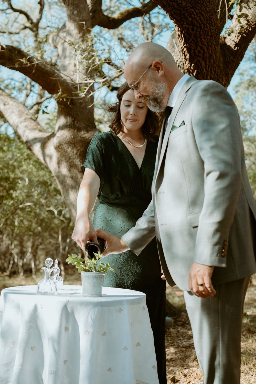 Intimate backyard wedding ceremony in Wimberley, TX, featuring a couple participating in a tree-planting unity tradition under oak tree