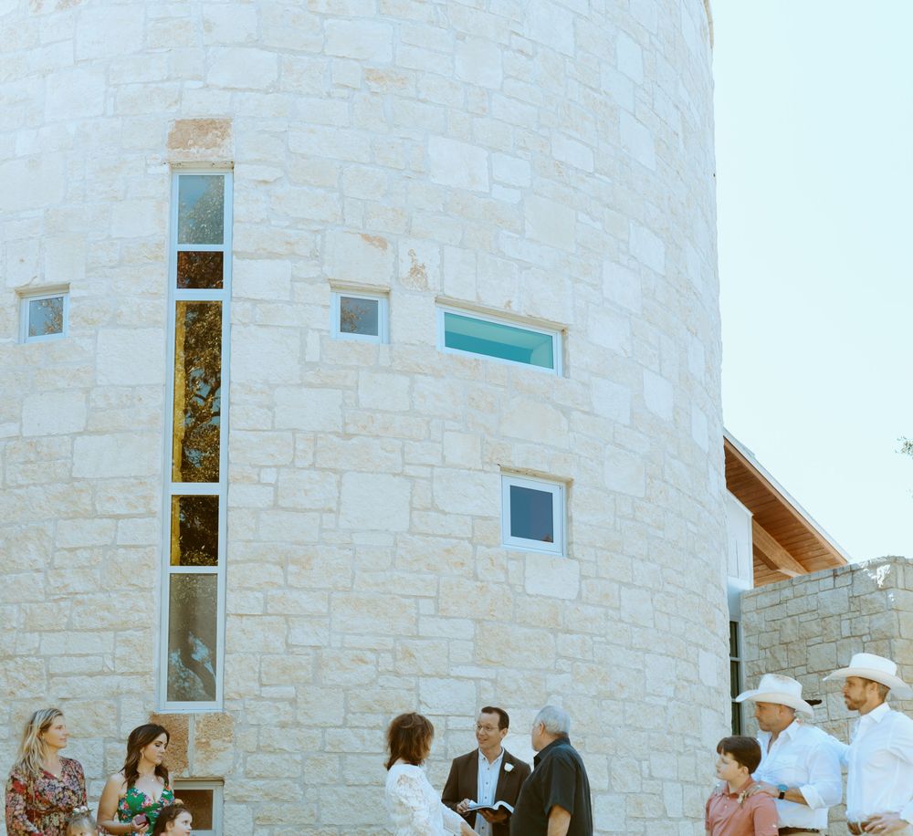 Outdoor wedding ceremony at a Texas Hill Country venue, showing the wedding party gathered by a limestone structure in Wimberley, TX.
