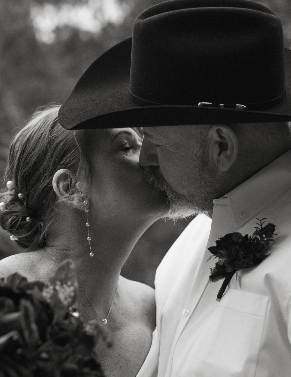 Close-up black and white wedding portrait of a bride and a groom wearing a cowboy hat kissing during an outdoor ceremony in Wimberley, Texas