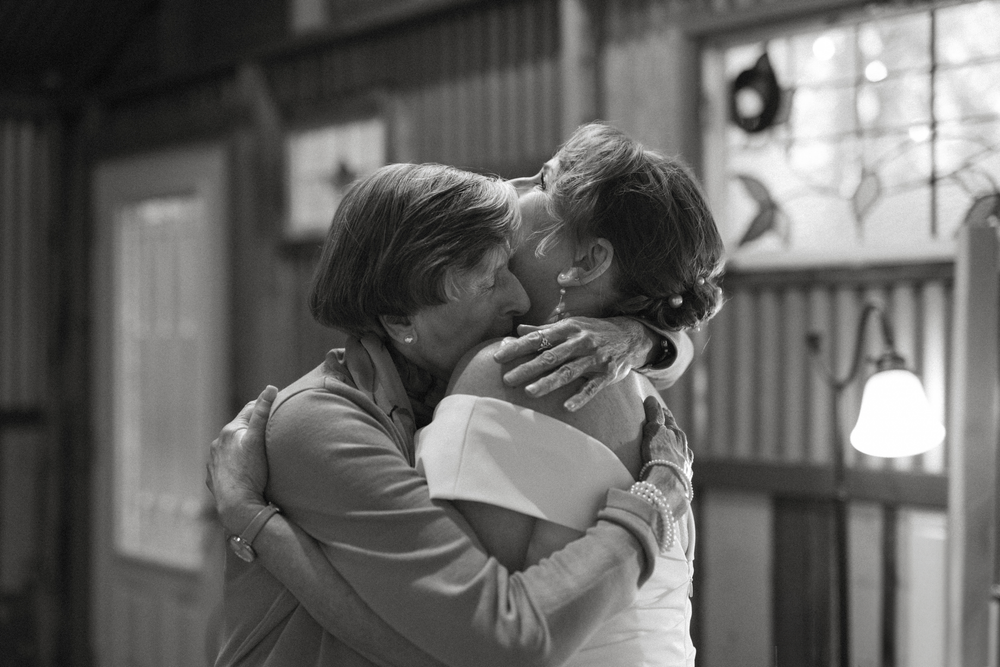 Candid black and white portrait of a bride hugging a loved one tightly at a rustic wimberley wedding venue.