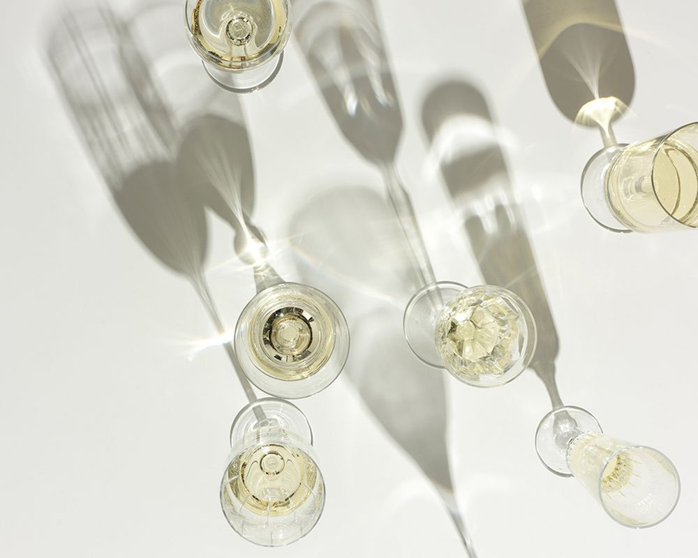 Overhead view of elegant champagne flutes casting long shadows on a white surface, filled with sparkling white wine.