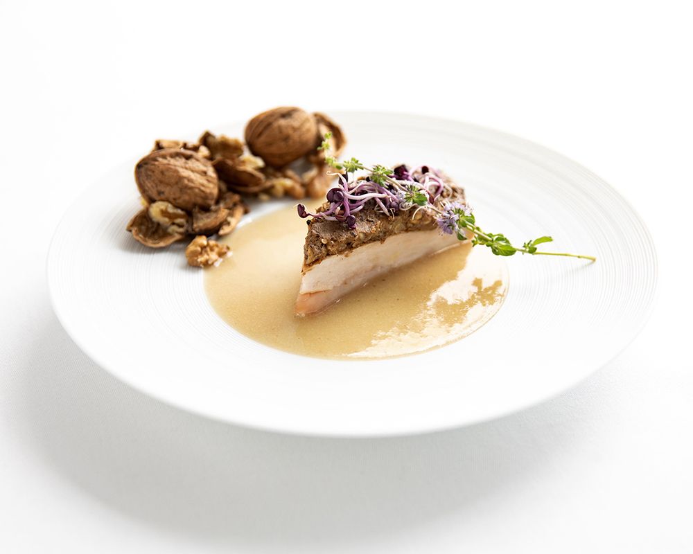 Elegant fine dining dish with seared fish, mushrooms, microgreens, and golden broth on a white plate.