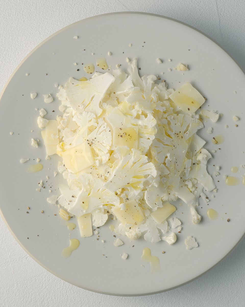 White cheese shavings with olive oil and black pepper on a gray ceramic plate.