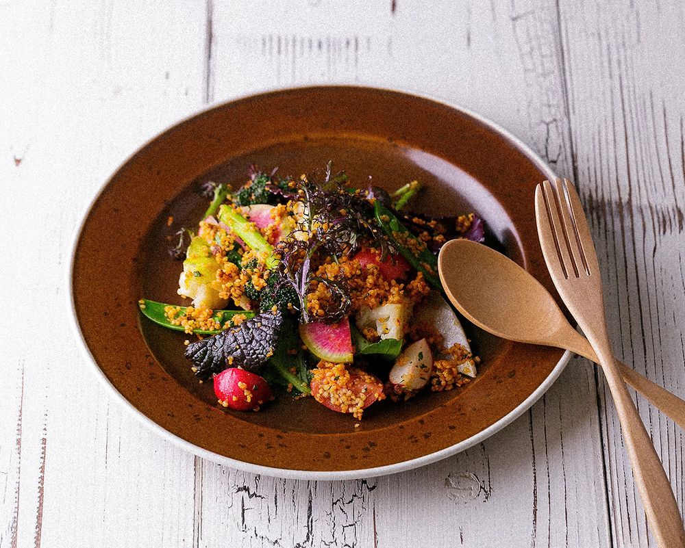 Colorful gourmet salad with fresh vegetables, herbs, and quinoa served on a rustic brown plate with wooden cutlery.