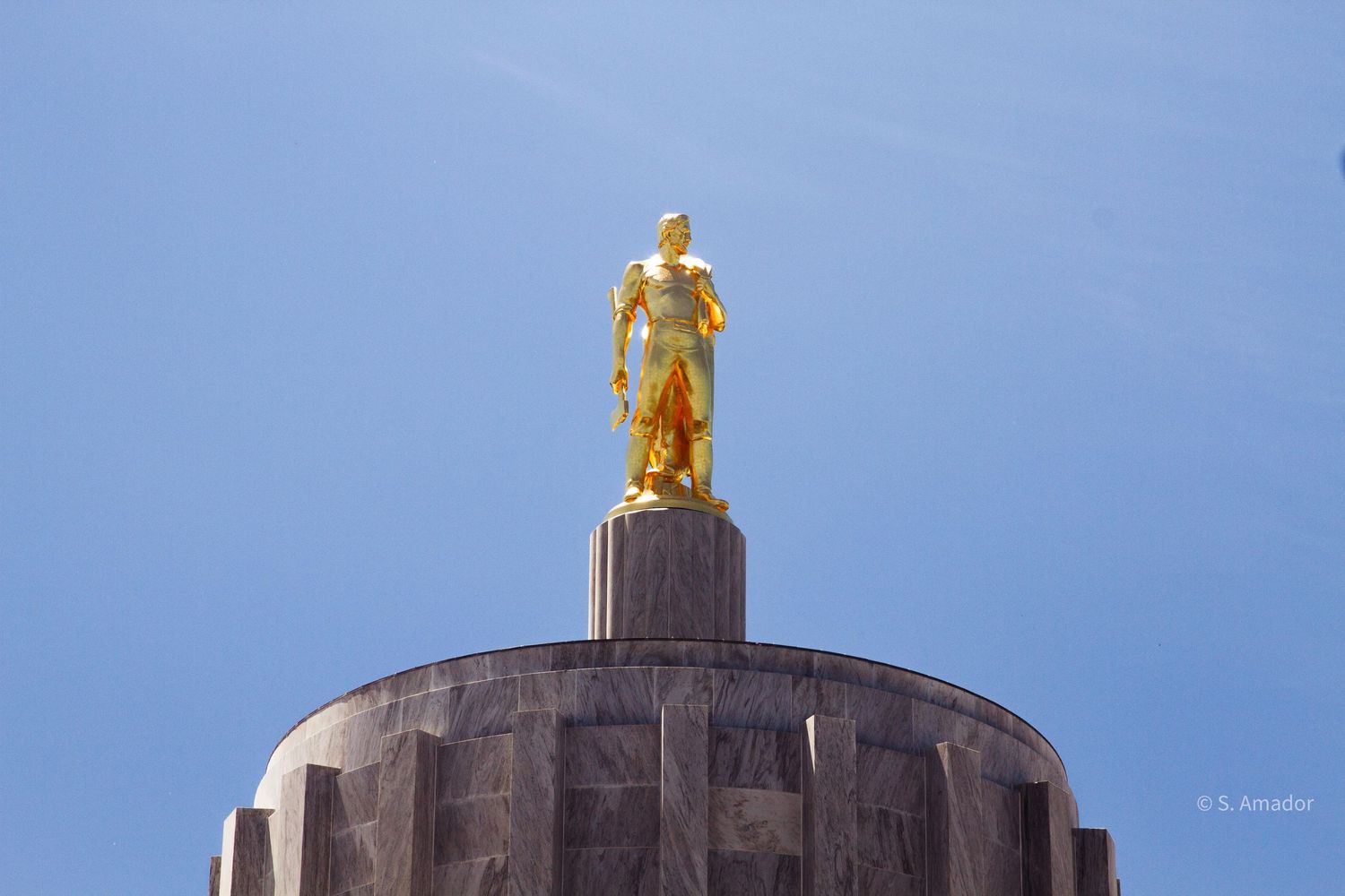 Golden statue atop the Oregon State Capitol building dome against a clear blue sky.