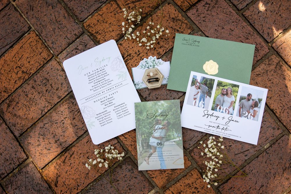 Wedding stationery suite with green envelope, invitation cards, and baby's breath flowers on brick pavers.