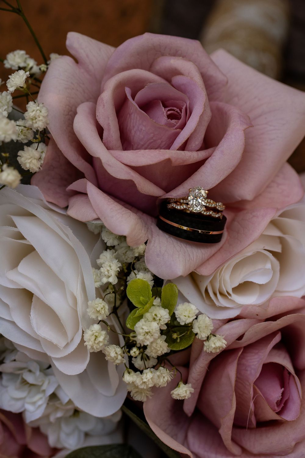 Wedding rings nestled inside a dusty pink rose surrounded by white roses and baby's breath bouquet.
