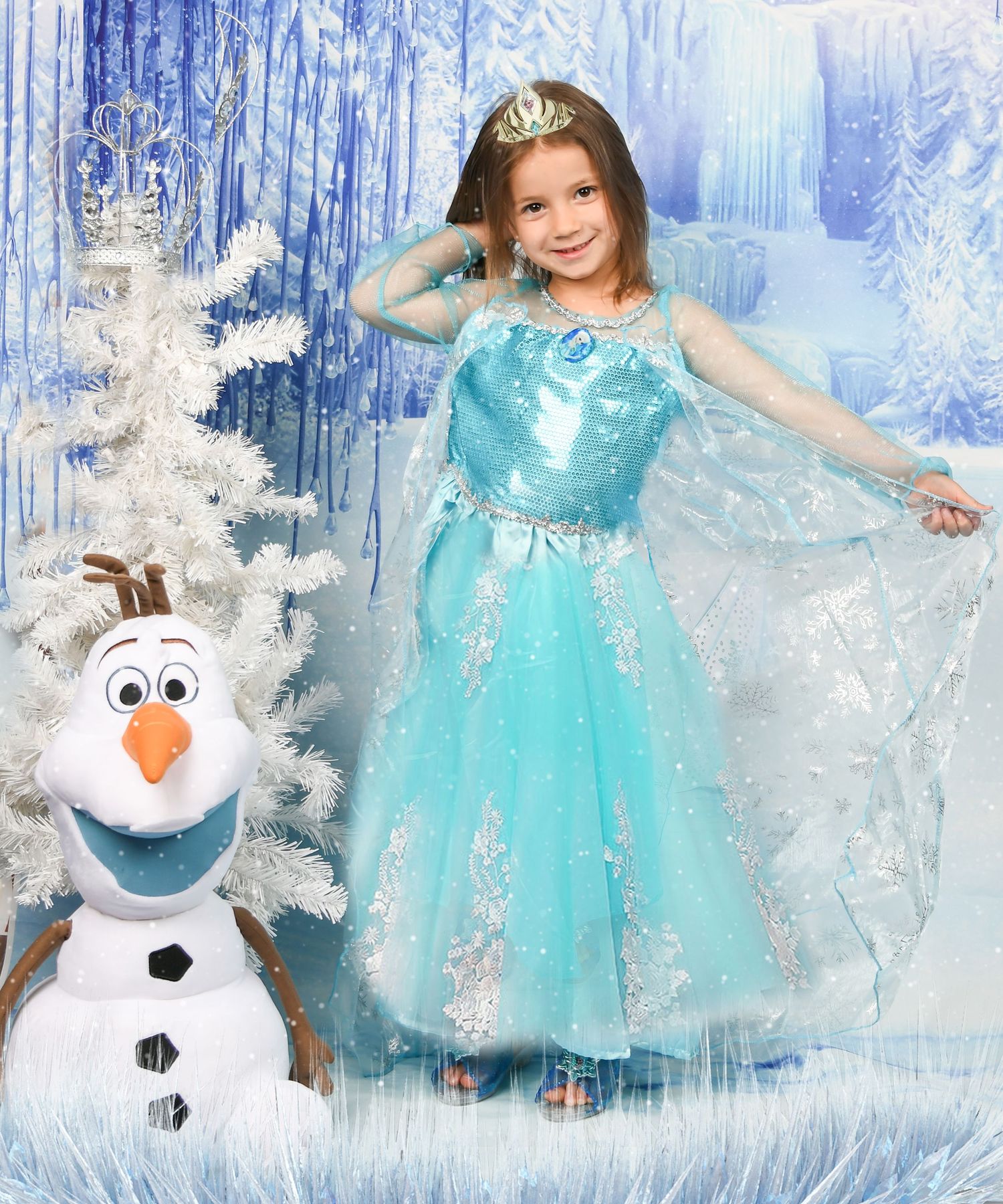 Girl in Elsa Frozen costume with tiara poses next to Olaf snowman figure in winter wonderland setting.