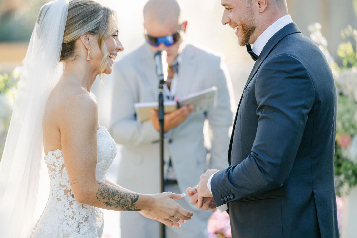 Armour House Wedding - Bride and groom exchange rings during outdoor wedding ceremony with officiant in background.