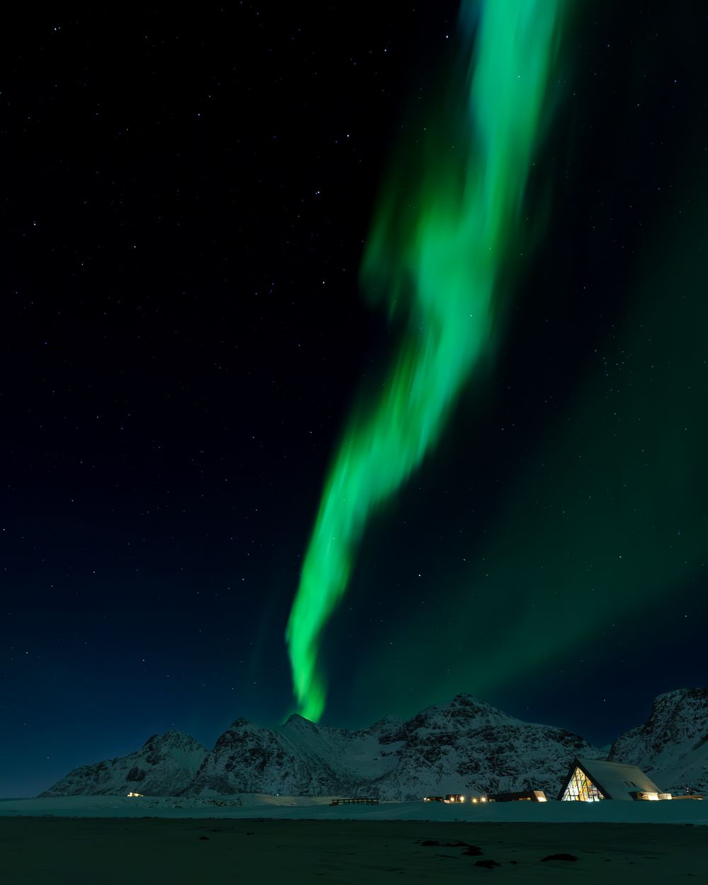 Brilliant green northern lights aurora borealis streak across the night sky above a snow-covered arctic landscape.