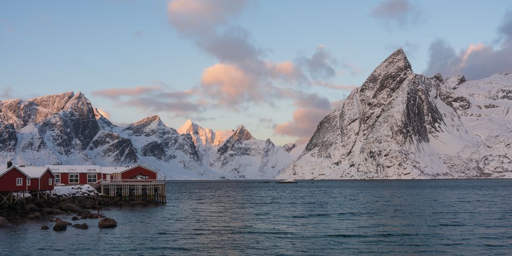 Traditional red Norwegian rorbu fishing cabins on stilts overlooking a serene fjord with snow-dusted mountains.
