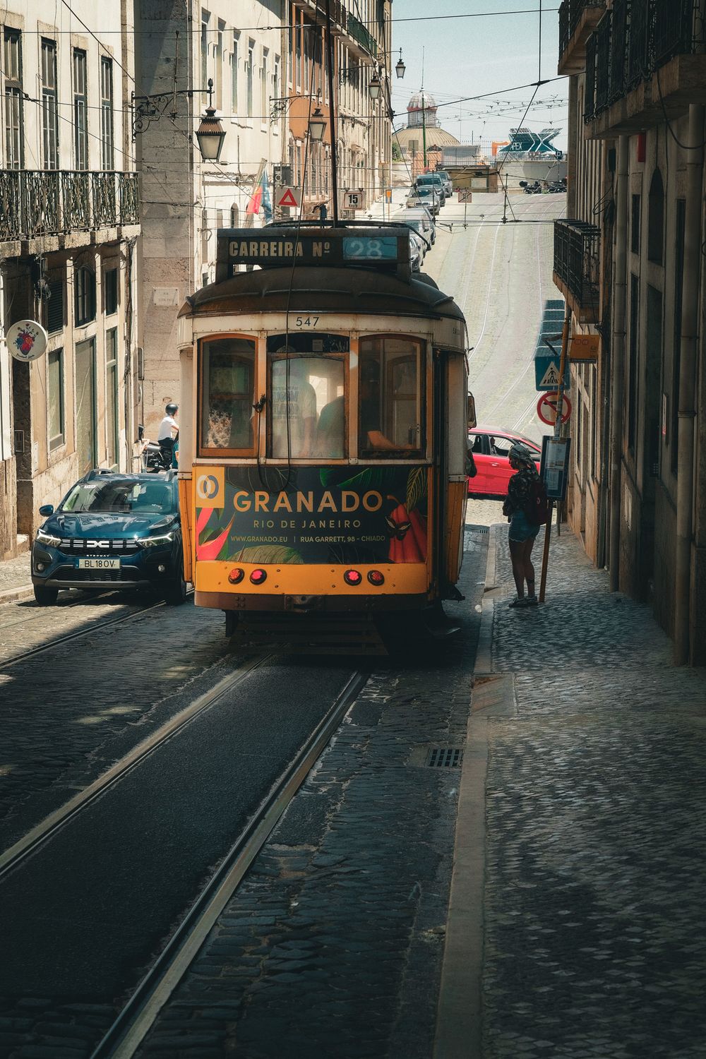 Yellow tram 28 with Granado Rio de Janeiro ad travels cobblestone street in Lisbon, Portugal.