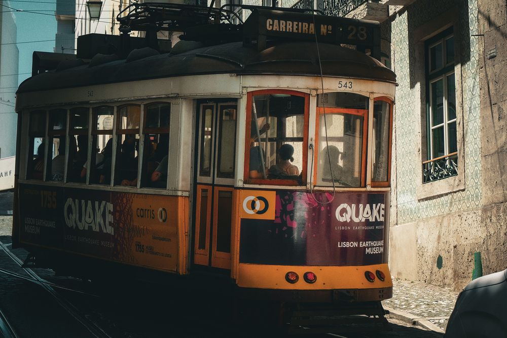 Yellow vintage tram with Quake advertisement navigating narrow Lisbon streets in Portugal.