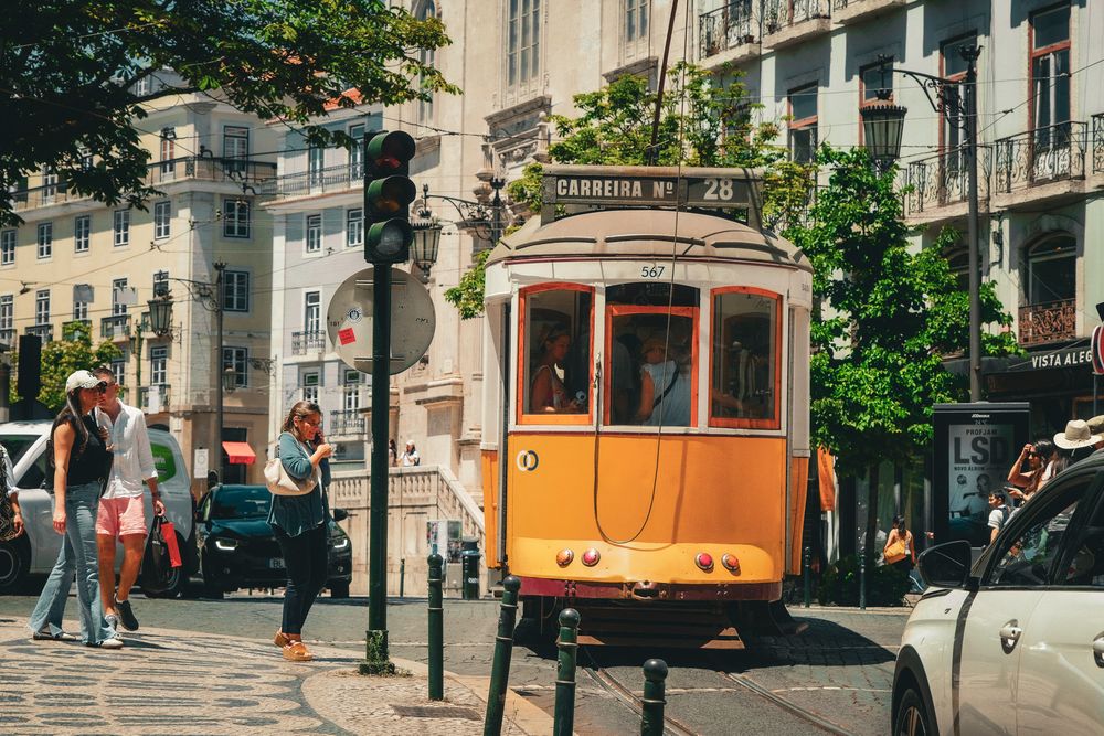 Vintage orange tram number 28 on a sunny Lisbon street with pedestrians and historic buildings in the background.