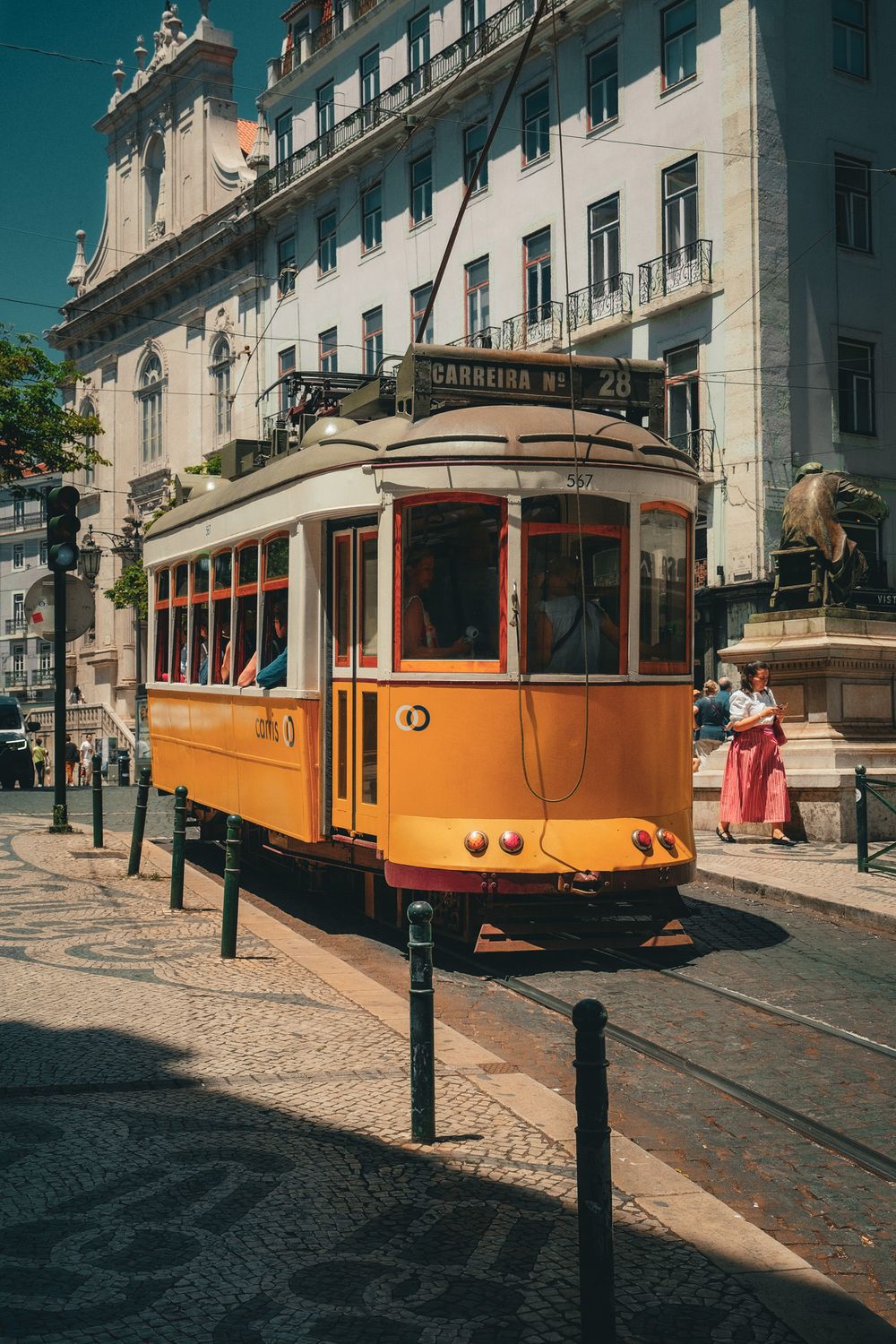Iconic yellow tram 28 on cobblestone streets of Lisbon, Portugal, with historic buildings and pedestrians in background.
