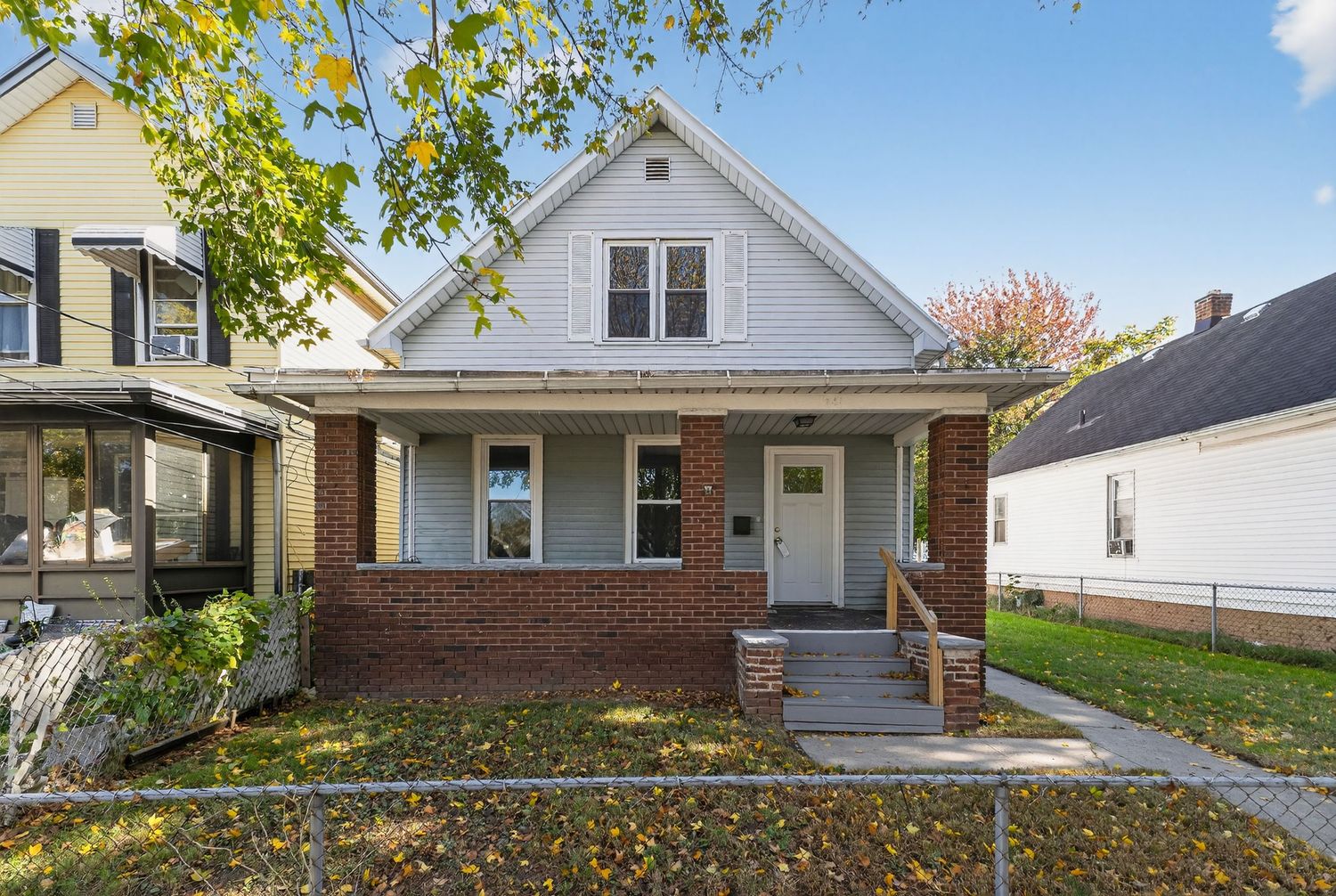Charming white clapboard bungalow with covered front porch, brick garage, and small front yard.