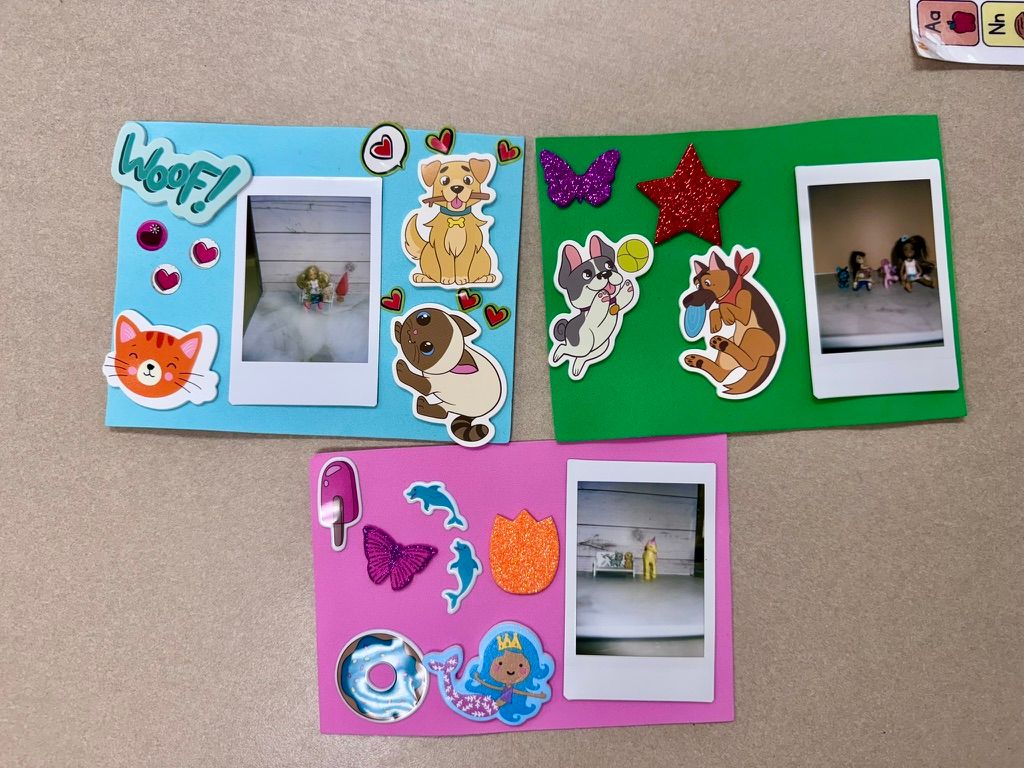 Handmade photo frames decorated with colorful stickers featuring animals, stars, and shapes, holding Instax photos on a beige surface.
