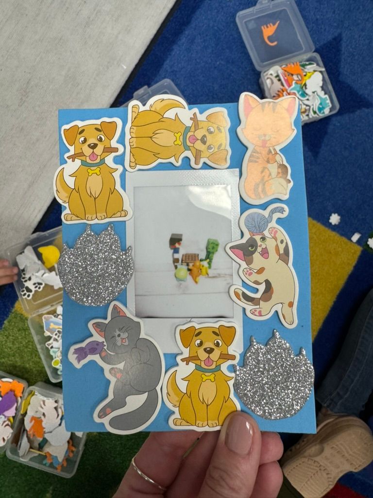 A handmade blue picture frame decorated with colorful cat and dog stickers and silver glitter accents held by a person.