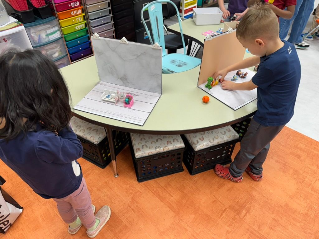 Two young children working at a colorful classroom table with school supplies in an elementary classroom.