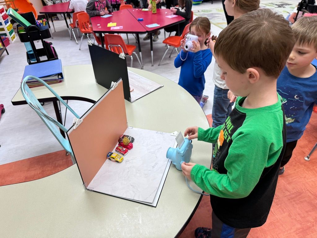 Young students engage in a hands-on science experiment with toy cars and ramps in a colorful elementary school classroom.