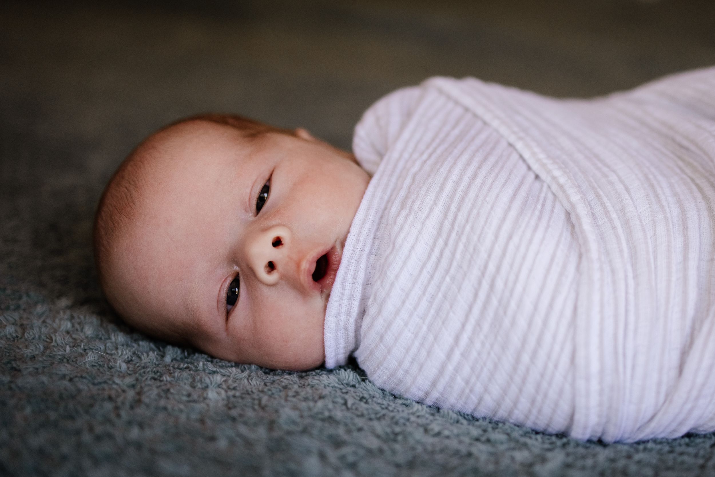 A close-up of a swaddled baby looking into the camera