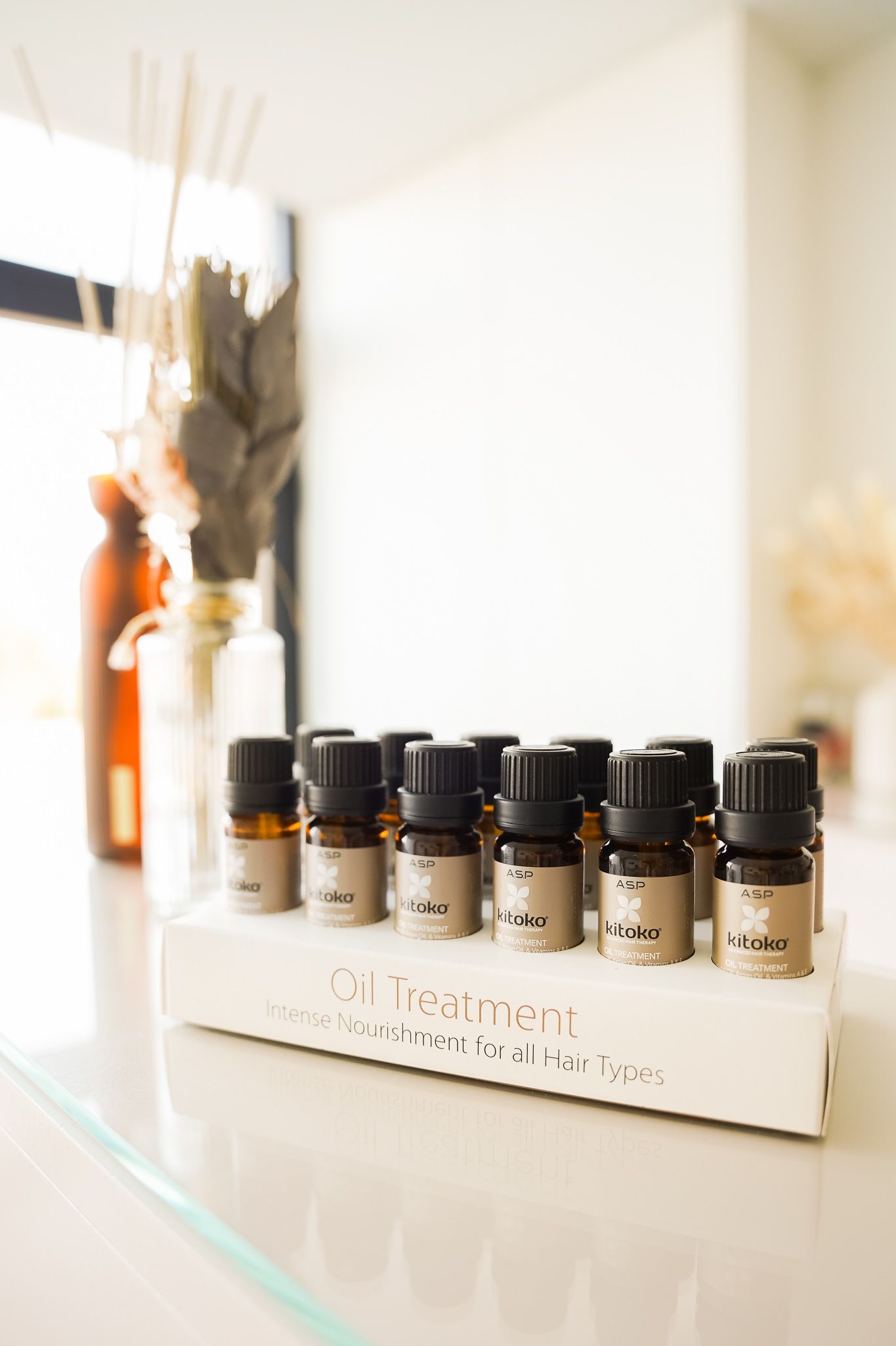 Row of essential oil bottles in a wooden holder with decorative elements in background.