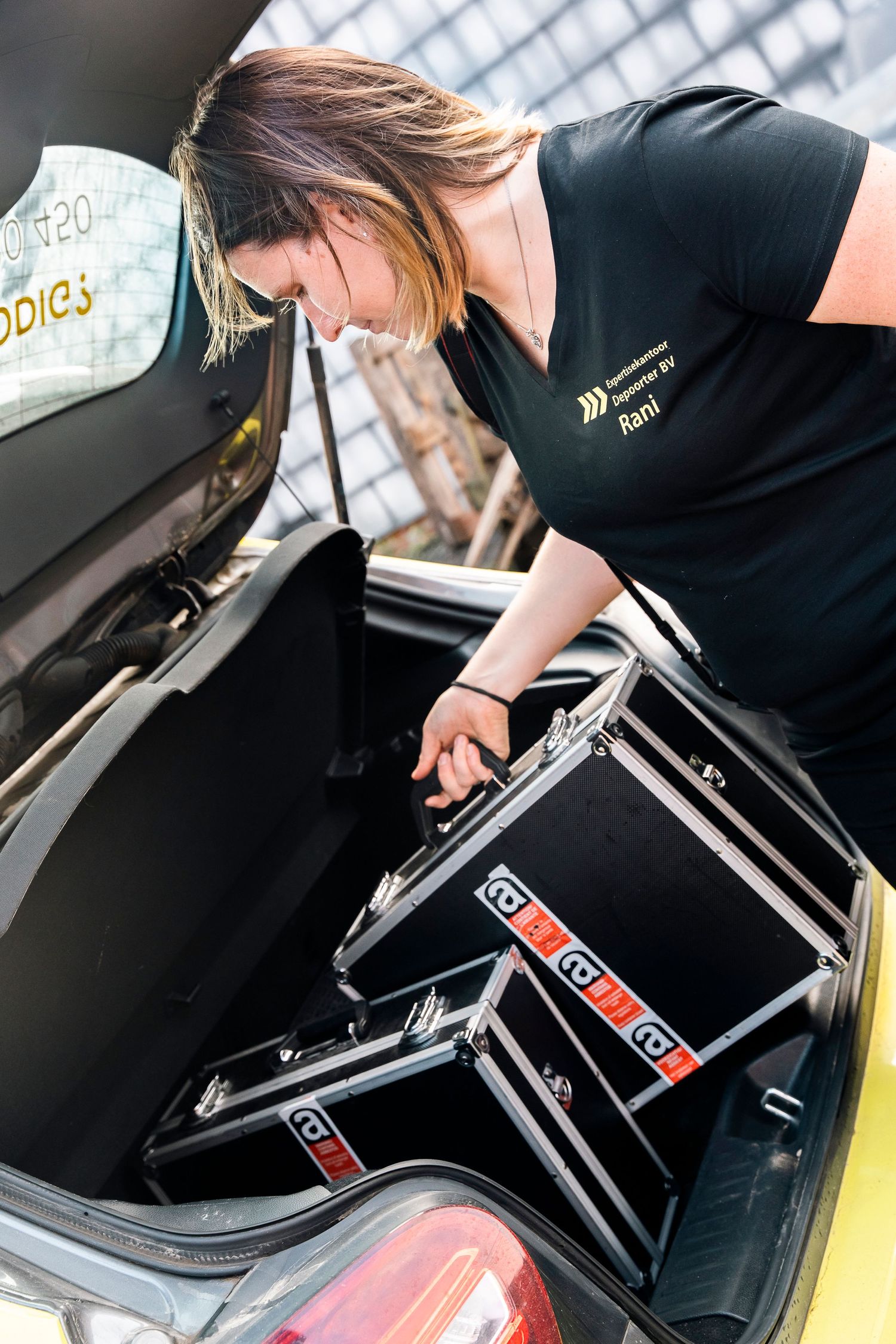 Professional loading equipment cases into vehicle trunk while wearing company uniform.