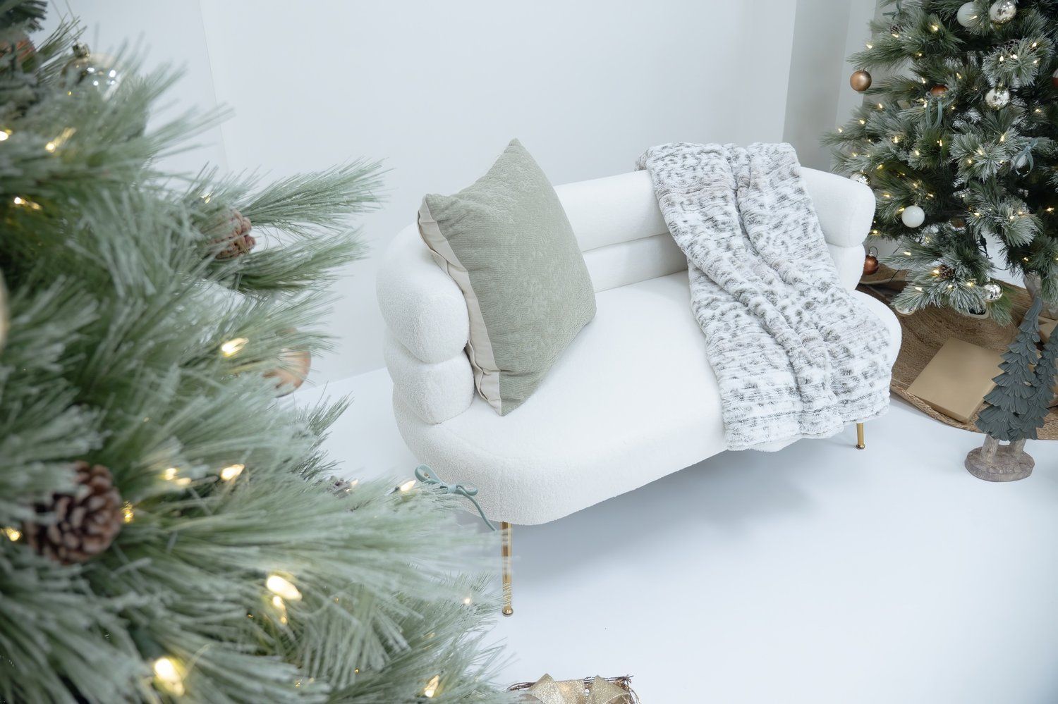 Cozy white sofa with grey pillow and throw blanket next to decorated Christmas tree.